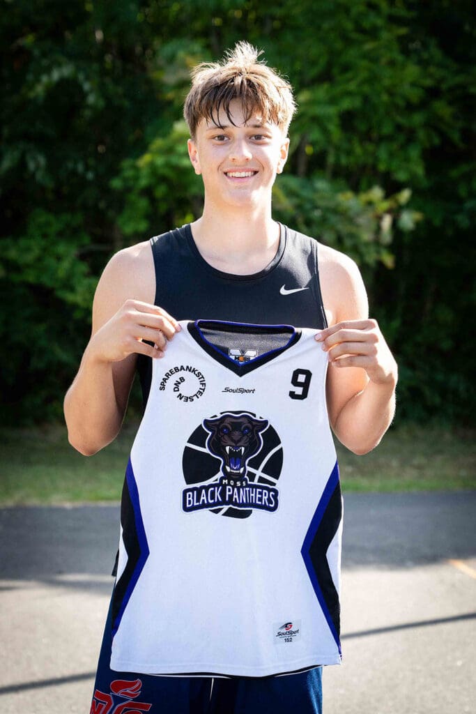 Fabian smiler mens han holder opp en litt for liten Moss Black Panthers basketballtrøye i Moss basketballklubb.